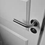 Close-up of a sleek steel door handle on a white door, showcasing modern interior design in monochrome.
